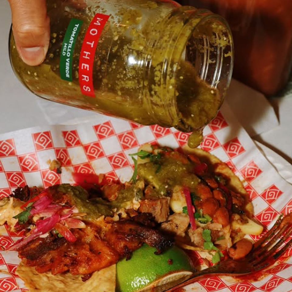 Pouring green salsa over tacos.