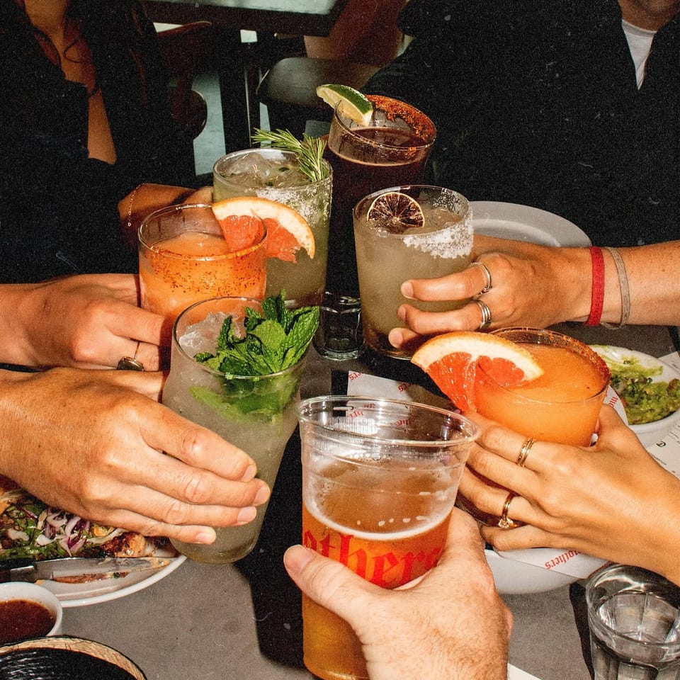 Friends raising cocktails and beer around a table.