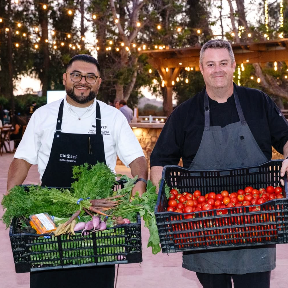two chefs holding crates of fresh vegetables