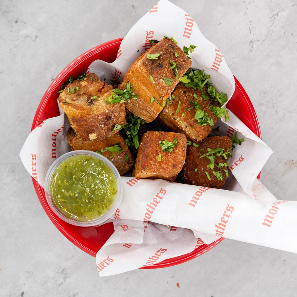 Crispy golden fried bites topped with chopped herbs in a red basket, served with green dipping sauce.