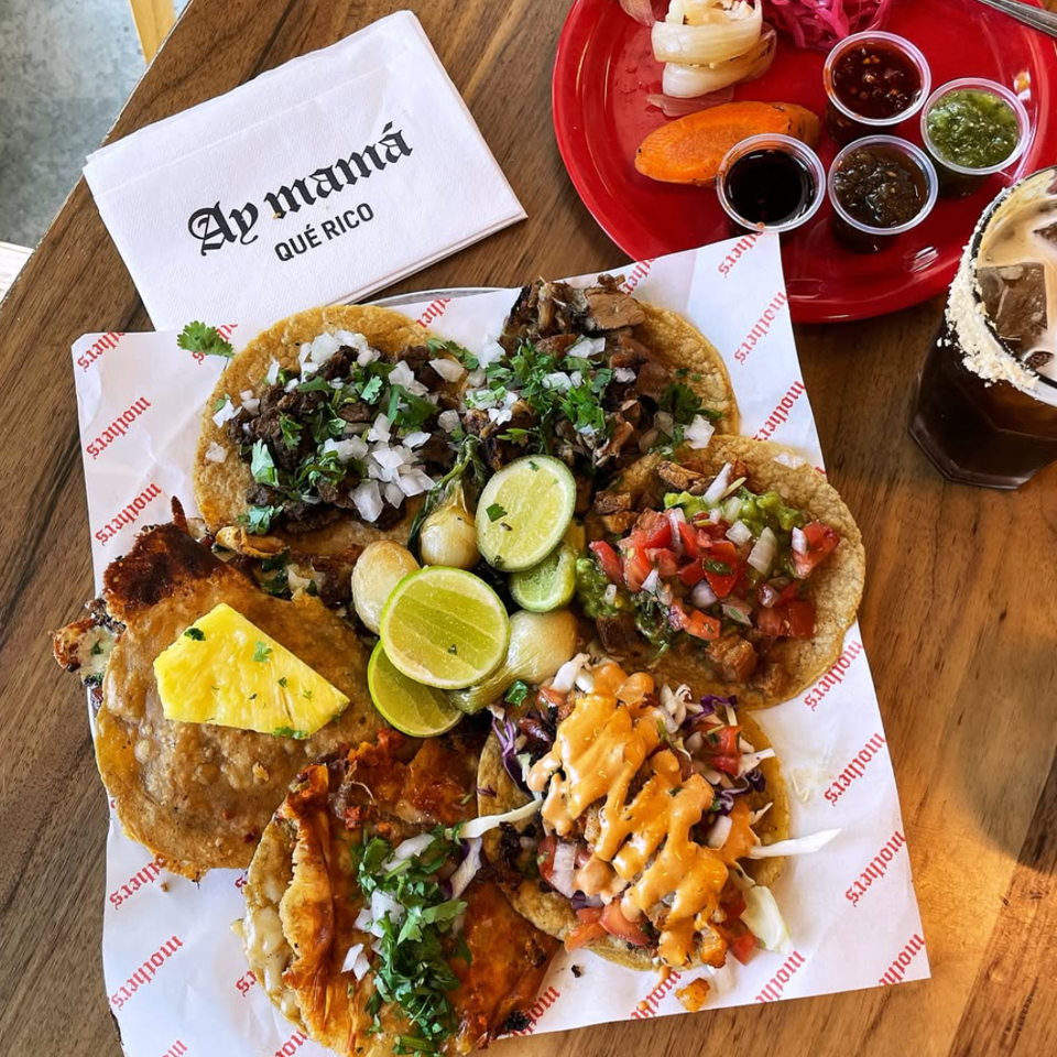 Assorted tacos with lime, salsas, and grilled vegetables on a wooden table.