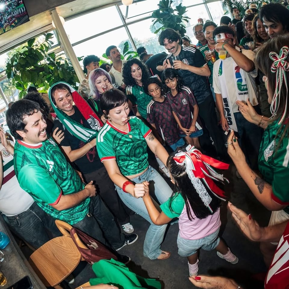 Crowded restaurant gathering where soccer fans in colorful jerseys celebrate together beneath hanging lights and tropical plants.